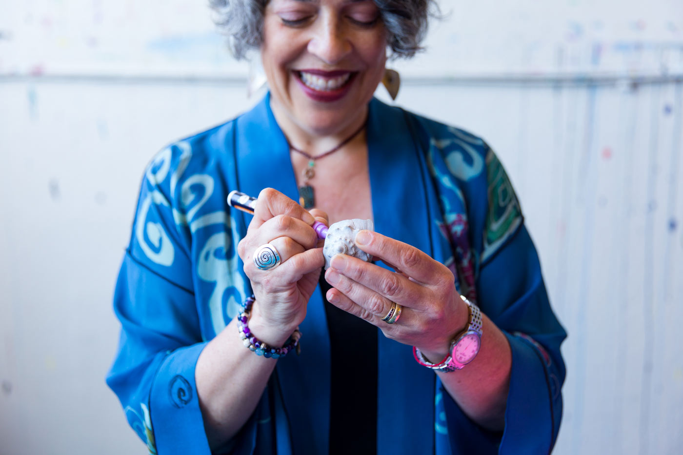 Photo: Karen Erlichman in a vibrant blue  smock, smiling as she decorates a shell.